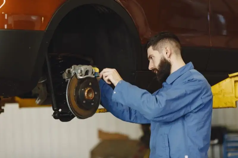 A mechanic in blue overalls working on a brake caliper with the wheel removed